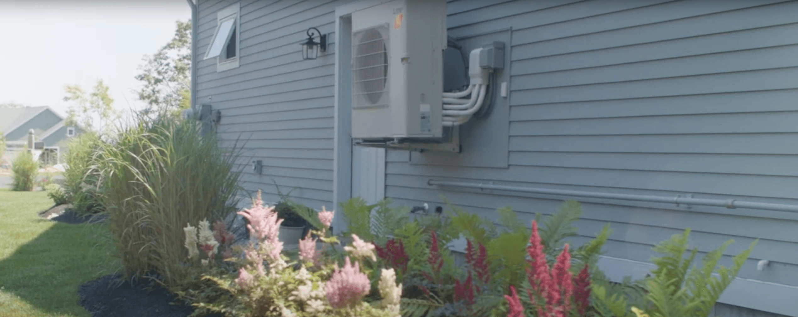 Outdoor Heat Pump Affixed to Blue House Over Garden